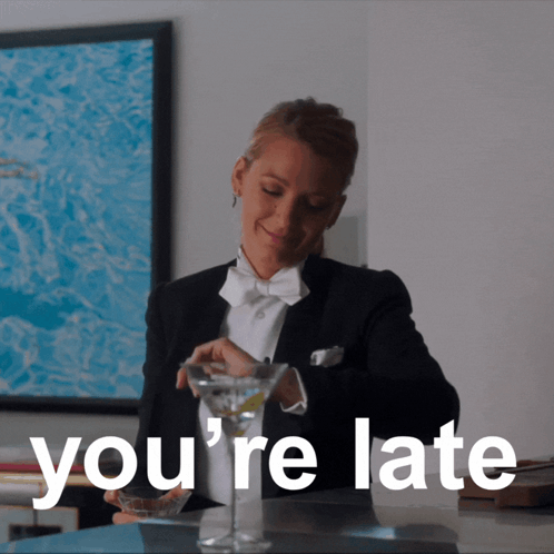 A Woman In A Tuxedo Is Pouring A Martini Into A Glass With The Words You 'Re Late Behind Her GIF