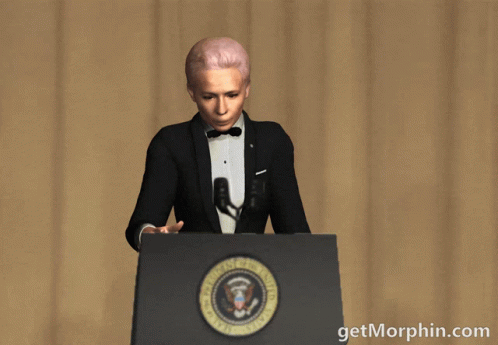 A Woman In A Tuxedo Stands At A Podium Holding A Microphone With The Words Getmorphin.com Written Below Her GIF
