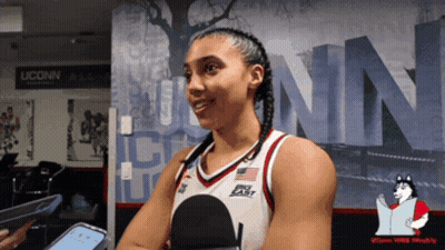 A Woman In A Uconn Basketball Uniform Is Talking Into A Microphone GIF
