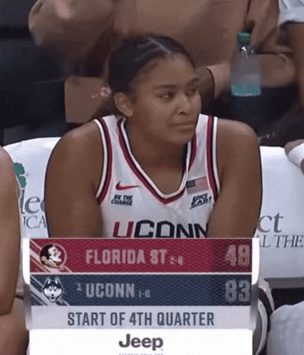 A Woman In A Uconn Jersey Sits In The Stands Watching A Game GIF