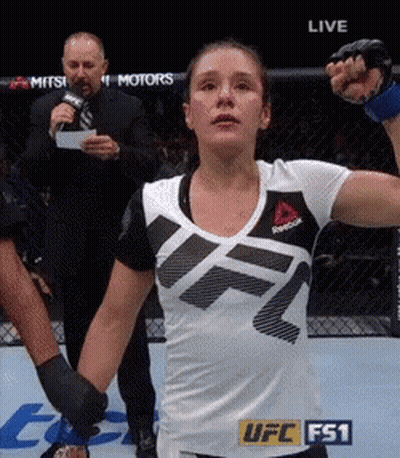A Woman In A Ufc Fs1 Shirt Holds Her Fist Up In The Air GIF