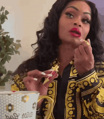 A Woman In A Versace Jacket Is Applying Lipstick To Her Lips GIF