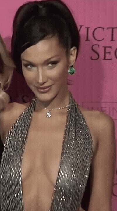 A Woman In A Very Plunging Dress Is Standing In Front Of A Pink Background That Says Victoria 'S Secret GIF