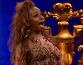 A Woman In A Very Revealing Dress Is Standing In Front Of A Gold Vase . GIF
