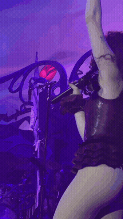 A Woman In A Very Revealing Outfit Is Singing Into A Microphone On Stage GIF