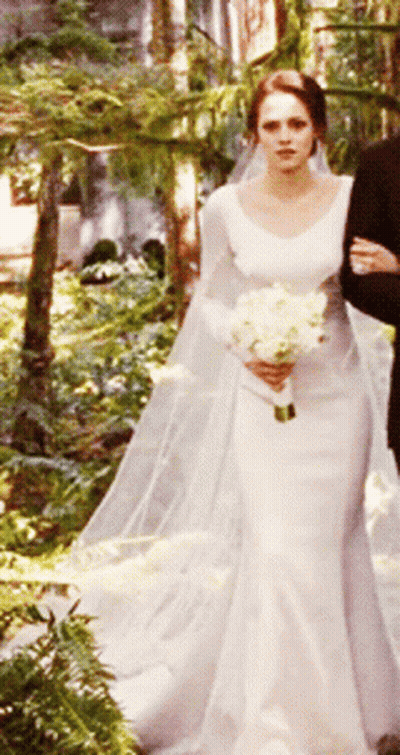 A Woman In A Wedding Dress Holding A Bouquet Of Flowers GIF