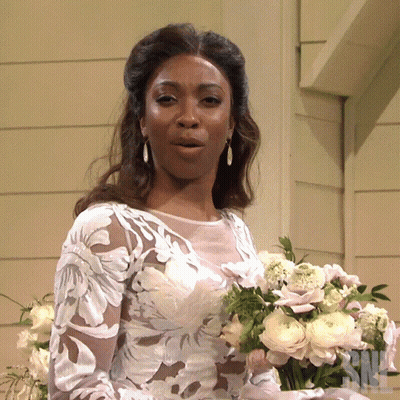 A Woman In A Wedding Dress Holds A Bouquet Of Flowers In Front Of A Sign That Says Nbc GIF