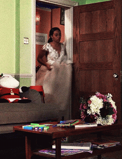 A Woman In A Wedding Dress Is Walking Out Of A Doorway GIF
