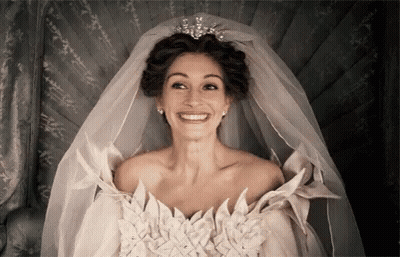 A Woman In A Wedding Dress With A Veil And Tiara Is Smiling . GIF
