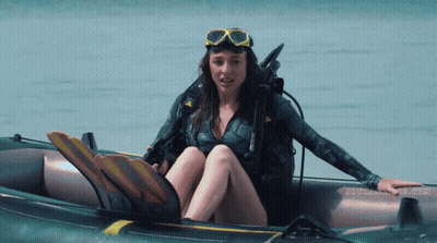 A Woman In A Wet Suit Is Sitting In An Inflatable Boat With The Word Scuba On The Bottom GIF