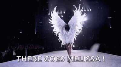 A Woman In A White Angel Costume Is Walking Down A Runway With The Words `` There Goes Melissa '' . GIF