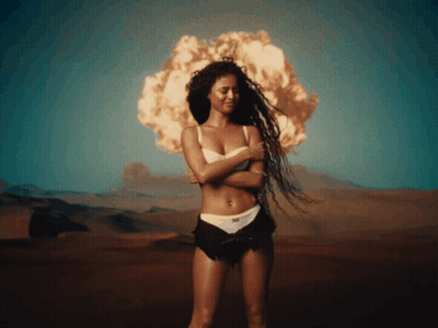 A Woman In A White Bra And Black Shorts Is Standing In Front Of An Explosion GIF
