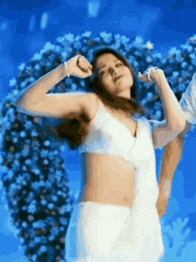 A Woman In A White Bra And White Skirt Is Dancing In Front Of A Flower Arrangement . GIF