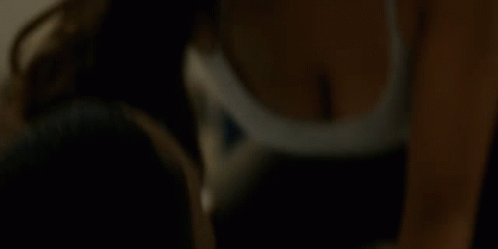 A Woman In A White Bra Is Sitting On A Bed Looking Down . GIF