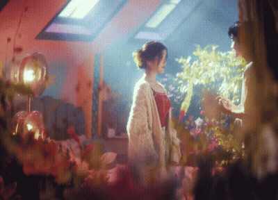 A Woman In A White Cardigan Stands Next To A Woman In A Red Top GIF