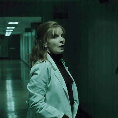 A Woman In A White Coat Stands In A Hallway GIF