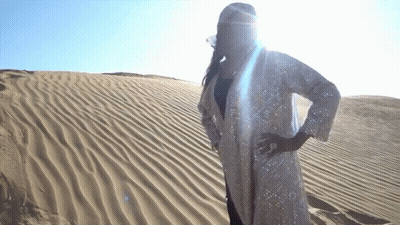 A Woman In A White Coat Stands In The Sand GIF