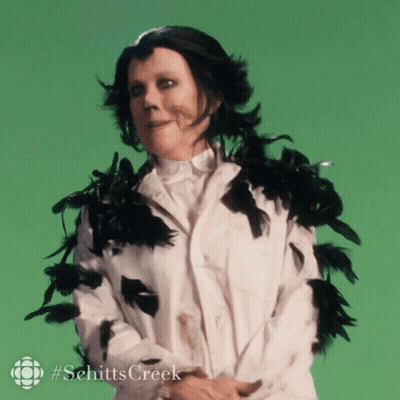 A Woman In A White Coat With Black Feathers Around Her Neck And Collar GIF