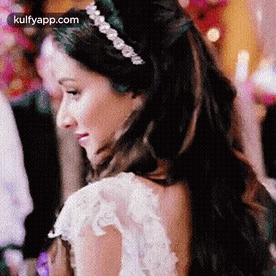 A Woman In A White Dress And A Headband Is Looking Over Her Shoulder . GIF