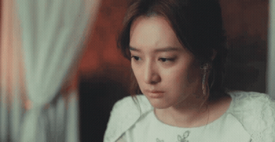 A Woman In A White Dress And Earrings Is Looking Down GIF
