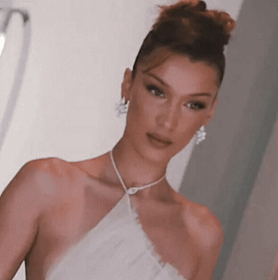 A Woman In A White Dress And Earrings Is Standing In A Room . GIF
