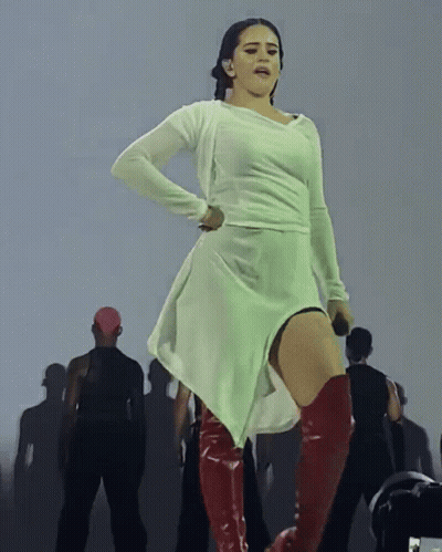 A Woman In A White Dress And Red Boots Is Standing On A Stage GIF