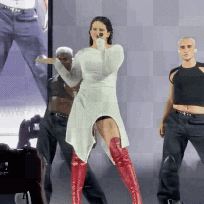 A Woman In A White Dress And Red Boots Sings Into A Microphone On Stage GIF