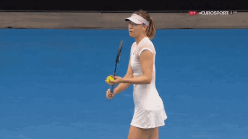 A Woman In A White Dress And Visor Is Playing Tennis On A Blue Court . GIF