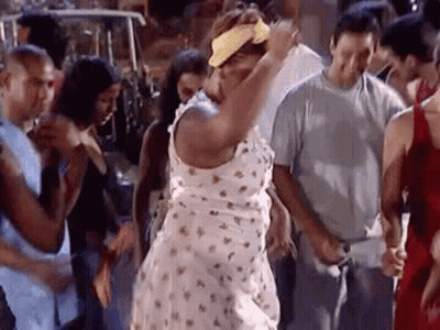 A Woman In A White Dress And Yellow Headband Is Dancing In A Crowd Of People . GIF