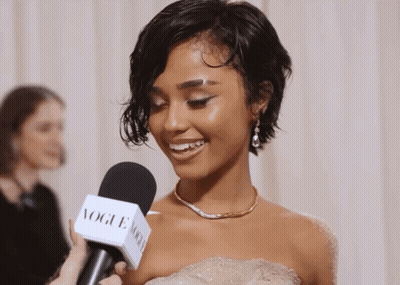 A Woman In A White Dress Is Being Interviewed By A Vogue Microphone GIF