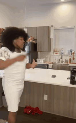 A Woman In A White Dress Is Dancing In A Kitchen GIF
