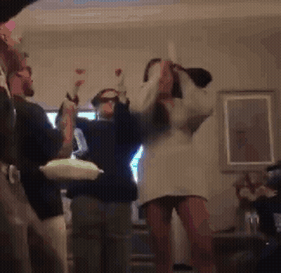 A Woman In A White Dress Is Dancing In A Living Room With Other People . GIF