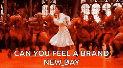 A Woman In A White Dress Is Dancing In Front Of A Crowd With The Words " Can You Feel A Brand New Day " Below Her GIF