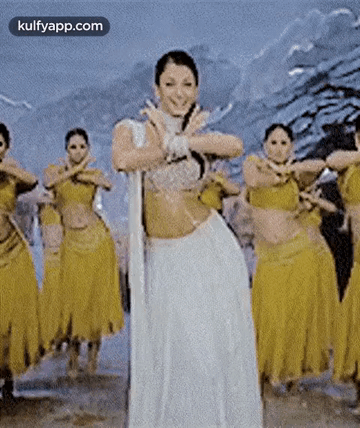 A Woman In A White Dress Is Dancing In Front Of A Group Of Dancers In Yellow Skirts . GIF