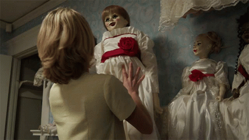 A Woman In A White Dress Is Holding A Doll With A Red Rose On It GIF