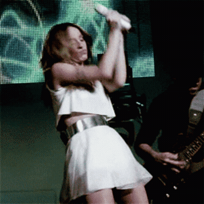 A Woman In A White Dress Is Holding A Microphone GIF