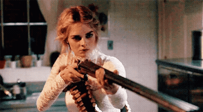 A Woman In A White Dress Is Holding A Shotgun In Her Hand . GIF