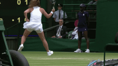 A Woman In A White Dress Is Holding A Tennis Racquet In Front Of A Scoreboard With The Number 1 On It GIF