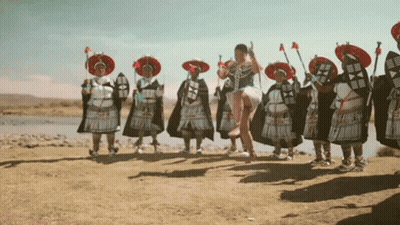 A Woman In A White Dress Is Jumping In The Air In Front Of A Group Of People In Traditional Costumes GIF