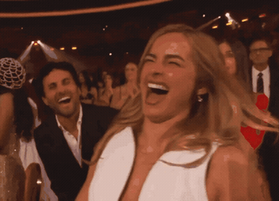 A Woman In A White Dress Is Laughing In A Crowded Room GIF