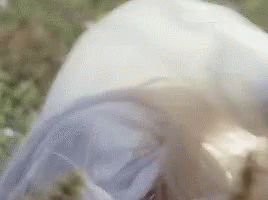 A Woman In A White Dress Is Laying In The Grass . GIF