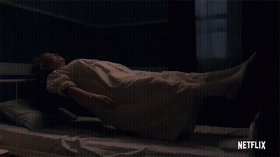 A Woman In A White Dress Is Laying On A Bed With A Netflix Logo Behind Her GIF