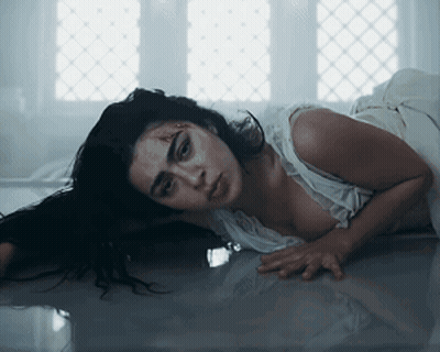 A Woman In A White Dress Is Laying On The Floor Looking At The Camera GIF