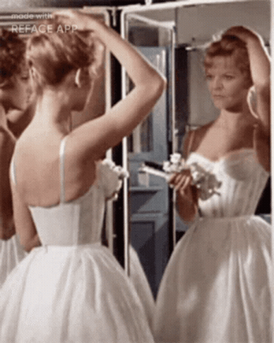 A Woman In A White Dress Is Looking At Her Reflection In A Mirror GIF
