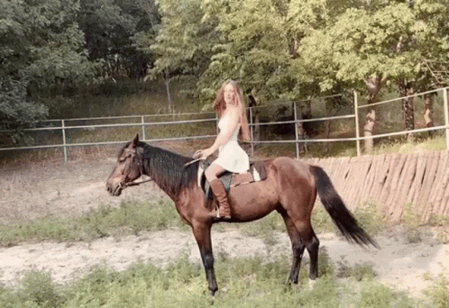 A Woman In A White Dress Is Riding A Horse In A Field . GIF