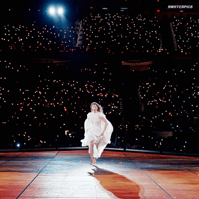 A Woman In A White Dress Is Running On A Stage With Swifterpics Written On The Bottom Of The Image GIF