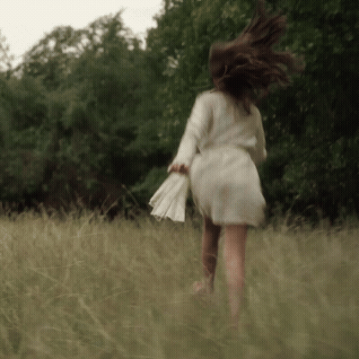 A Woman In A White Dress Is Running Through Tall Grass GIF
