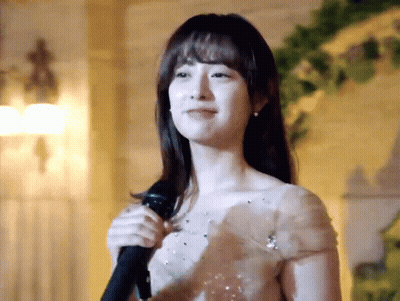 A Woman In A White Dress Is Singing Into A Microphone . GIF
