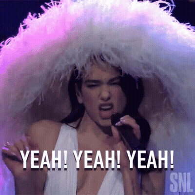 A Woman In A White Dress Is Singing Into A Microphone While Wearing A Feathered Hat . GIF