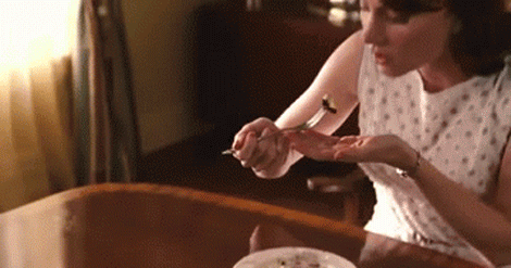 A Woman In A White Dress Is Sitting At A Table With A Plate Of Food GIF